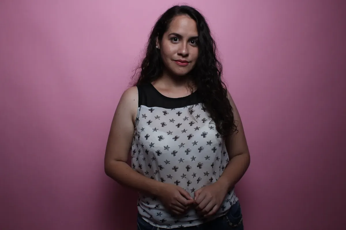 Confident woman with curly hair posing against a pink background.