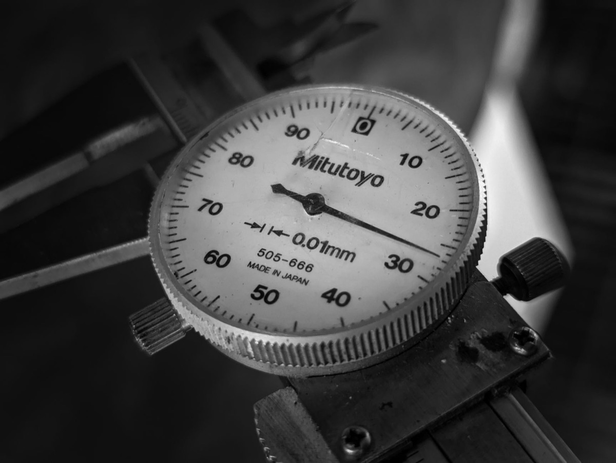 A detailed macro shot of a manual analog vernier caliper scale being read by a technician.