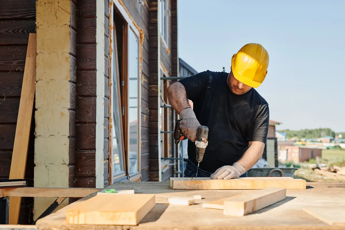 建築工人使用電鑽在建築工地，白天 outdoors。