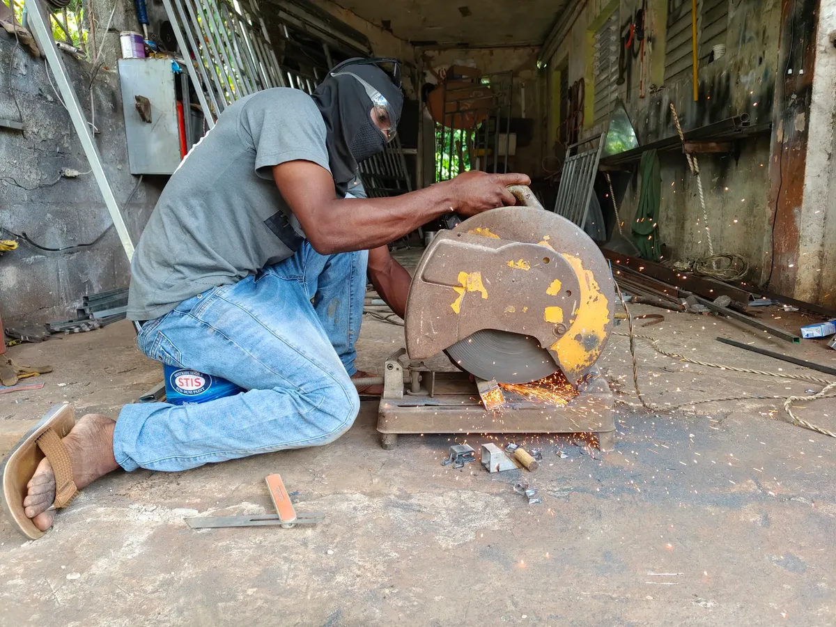 A worker uses a metal cutting saw in a workshop, creating sparks. Safety equipment is worn.
