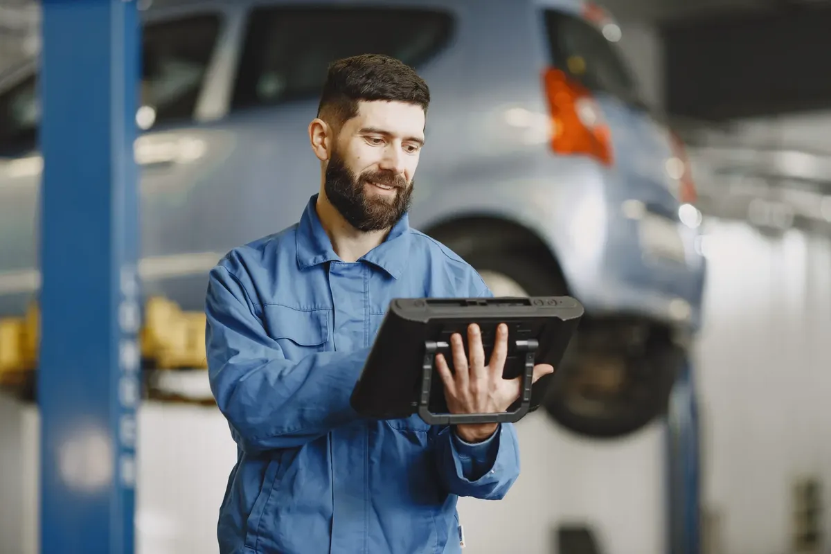 笑顔の自動車メカニクスが車修理店の環境でデジタルタブレットを使用している。